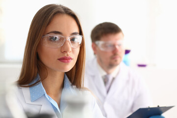 Fototapeta premium Two laboratory worker wearing white lab coats and special safety glasses while working together in the laboratory. Science and research concept