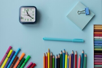 Set of school and office supplies on blue  background: pen, clips, note paper, colored pencils, crayons, felt-tip-pens and alarm clock. Concept: back to school. Flatlay, top view.