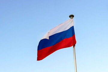 Fototapeta na wymiar The Russian flag on the flagpole flutters against a blue cloudless sky.
