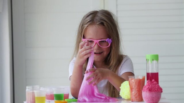 A little girl with glasses is played with a homemade pink slime. Kids hands playing slime toy. Making slime. Copyspace.
