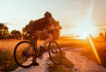  yclist on a bicycle looks at the sunset in the field. Beautiful evening landscape with a bicycle....