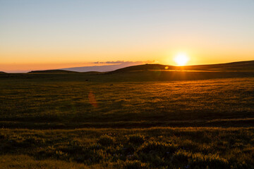 Beautiful sunset landscape. The green field and mountains illuminates the sun rays.
