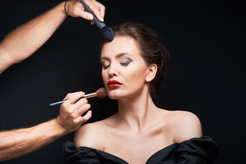 Obraz premium beautiful woman with beautiful brown hair in a dark dress on a dark background closed eyes and stylist does makeup