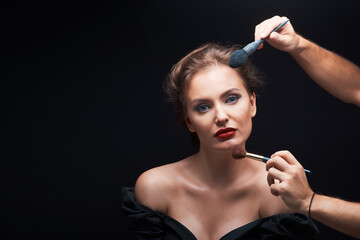 Obraz premium beautiful woman with beautiful brown hair in a dark dress on a dark background and the stylist does makeup