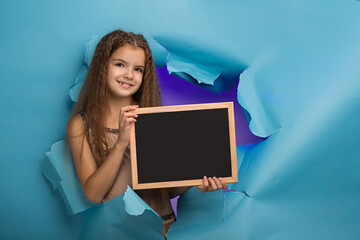 girl with a sign peeps into a hole in blue paper