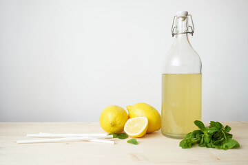 Lemonade in glass and bottle on wooden table. Lemonade or mojito cocktail with lemon and mint, cold refreshing drink or beverage with ice. Copy space for your text © YanaKho