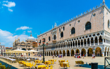 Fototapeta premium Venice, Italy - june 29th 2020 - very little tourists crossing the San Marco square and passing the empty terraces with the Saint Mark's Basilica and the Doge's Palace on a sunny Corona day in summer
