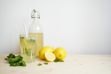 Lemonade in glass and bottle on wooden table. Lemonade or mojito cocktail with lemon and mint, cold refreshing drink or beverage with ice. Copy space for your text
