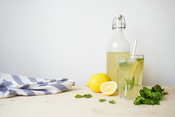 Lemonade in glass and bottle on wooden table. Lemonade or mojito cocktail with lemon and mint, cold refreshing drink or beverage with ice. Copy space for your text