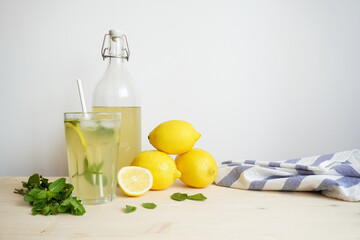 Lemonade in glass and bottle on wooden table. Lemonade or mojito cocktail with lemon and mint, cold refreshing drink or beverage with ice. Copy space for your text