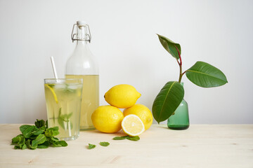 Lemonade in glass and bottle on wooden table. Lemonade or mojito cocktail with lemon and mint, cold refreshing drink or beverage with ice. Copy space for your text
