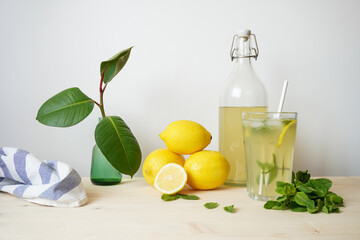 Lemonade in glass and bottle on wooden table. Lemonade or mojito cocktail with lemon and mint, cold refreshing drink or beverage with ice. Copy space for your text