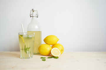 Lemonade in glass and bottle on wooden table. Lemonade or mojito cocktail with lemon and mint, cold refreshing drink or beverage with ice. Copy space for your text