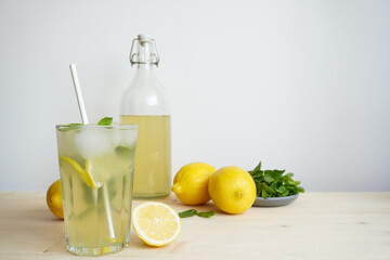 Lemonade in glass and bottle on wooden table. Lemonade or mojito cocktail with lemon and mint, cold refreshing drink or beverage with ice. Copy space for your text