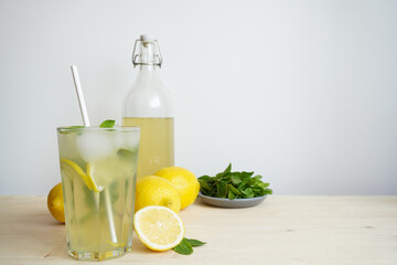 Lemonade in glass and bottle on wooden table. Lemonade or mojito cocktail with lemon and mint, cold...