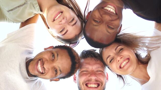 Close portrait of five young students, tolerance and no racism concept. Interracial group of students leaned over the camera against the sky