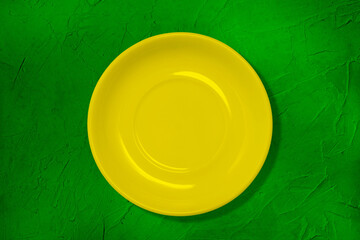 The plate on the table. Yellow empty plate on a green table with texture. The concept of cooking. Colored kitchen utensils. Minimal style. A top view of a flat layout.