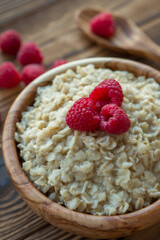 Oatmeal porridge with raspberry berries in a wooden bowl on a wooden background. Useful breakfast, diet.