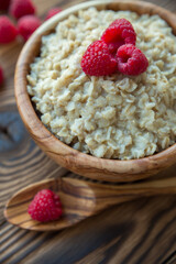 Oatmeal porridge with raspberry berries in a wooden bowl on a wooden background. Useful breakfast, diet.
