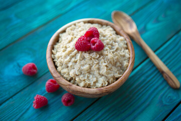 Oatmeal with raspberry berries in a wooden bowl on a blue background