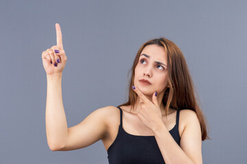 Fototapeta premium Asian and Turkish looking woman pointing up with her hands and in a thoughtful mood, studio shot with grey background