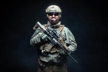 soldier in military equipment with a rifle smiles at night, a commando in uniform against a dark background, a portrait of a ranger