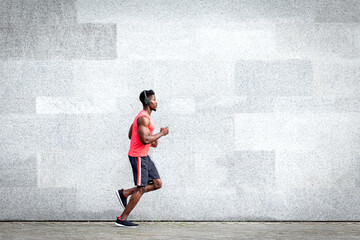 African American guy runner runs fast forward against the background of the city wall, sports man train on the street