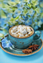 Cup of coffee with marshmallows and hydrangea flower on a blue background.