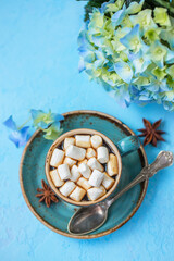 Fototapeta na wymiar Cup of coffee with marshmallows and hydrangea flower on a blue background.