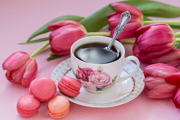 Cup of coffee with macaroons and tulips on a pink background.