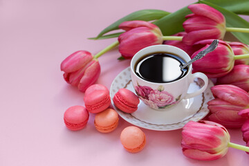 Fototapeta na wymiar Cup of coffee with macaroons and tulips on a pink background.