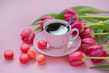 Pink cup of coffee with tulips and macaroons on a pink background. Concept