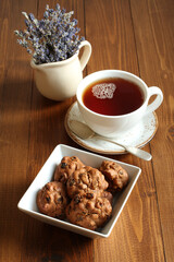 Chocolate cookies with walnuts and raisins in a square bowl and a cup of black tea on a wooden table. Closeup