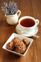 Chocolate cookies with walnuts and raisins in a square bowl and a cup of black tea on a wooden table. Closeup