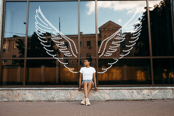 afro american woman sitting at the glass showcase with Angel wings on background