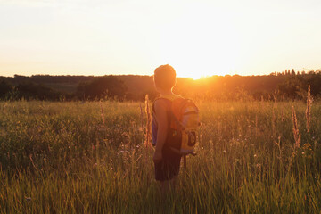   A boy with a backpack looks at the sunset
