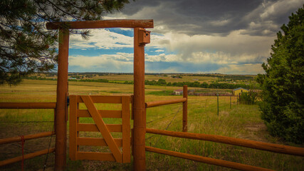 Log fence and gate with a bird house separating farmhouse back yard from livestock pasture and distant rolling prairie