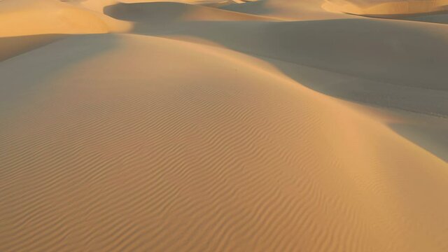 Beautiful aerial footage of sand hills peaks in golden sunrise light. Drone is flying over the scenic landscape of massive dunes at summer. 4K wild desert nature. Abstract wavy shapes and pattern