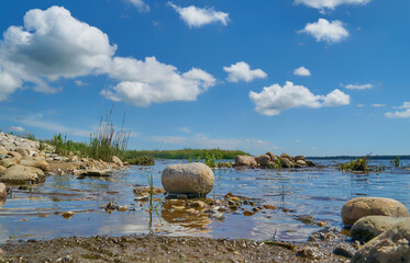 a stone is lying in the water of the lake Filsø on a sunny summer day against scenic blue sky with white clouds