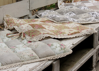 Fototapeta na wymiar Soft pillows with floral print on a white wooden bench in the loft style on the street, close-up