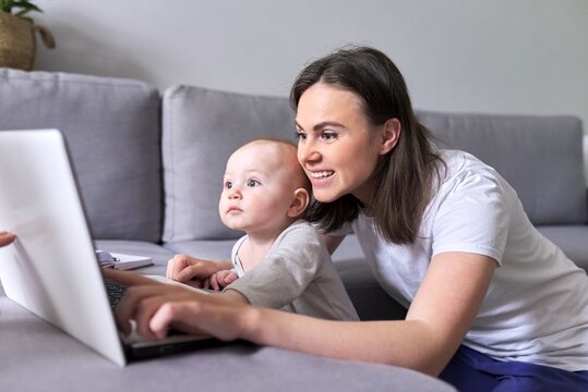 Young Smiling Mom With Toddler Baby Look Together At Laptop