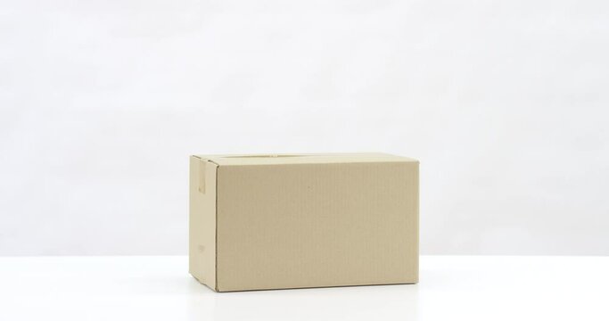 Cardboard box falls on white table. 6K slow motion shot on Red