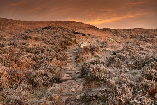 Devil's Staircase, part of the West Highland Way long distance walking route, in Glencoe, Scotland at sunset showing stone path, foliage with frost and dramatic sky