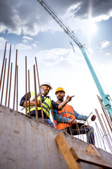 Men in hardhat and yellow and orange jacket posing on building site