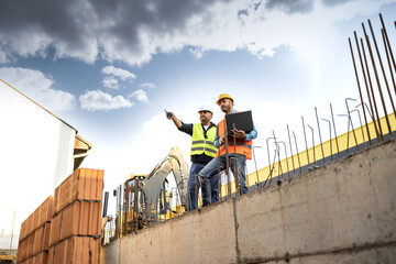 Men in hardhat and yellow and orange jacket posing on building site
