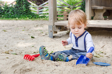 Fototapeta premium Cute little child having fun playing with sand and colorful toys in the park, beautiful summer sunny day in children playground