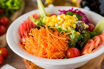 Healthy mixed salad in white bowl on wooden table.