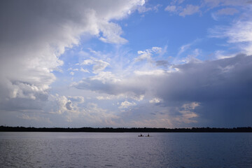 On a lake, a small rowboat drives in the distance under dark storm clouds