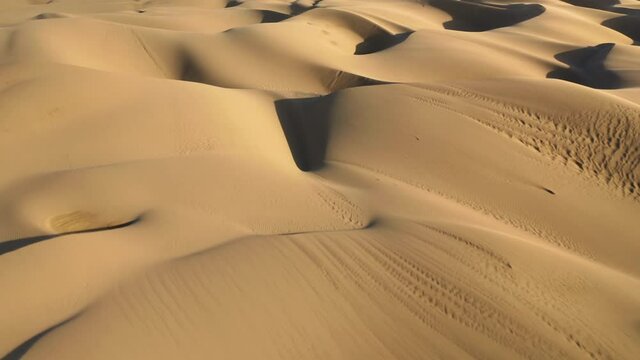 Wild desert nature, Africa. Magical aerial view from drone flying over the scenic landscape of massive beige dunes at sunset. 4K drone view on the abstract wavy shape and pattern on golden sand hills