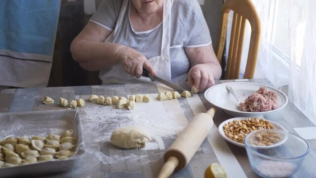 Beautiful elderly woman with wrinkled hands prepares dough on kitchen table. Knife, minced meat and condiments for pies. shallow depth of field